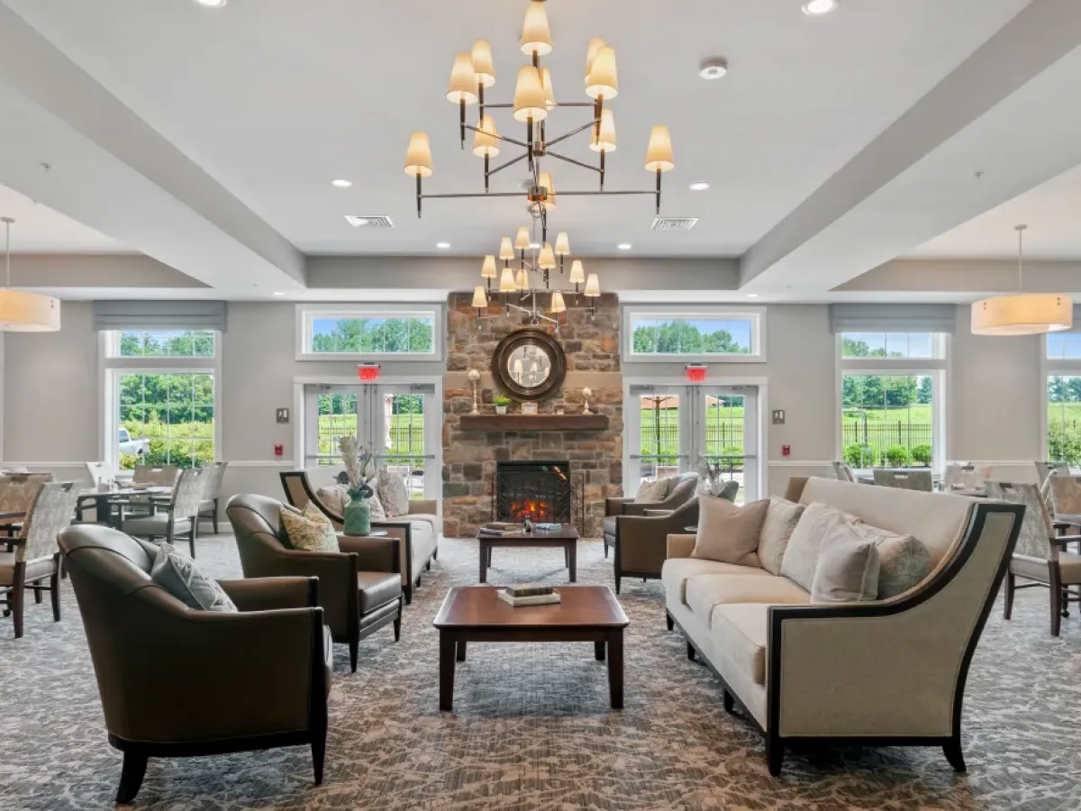 Westrum Corporate Elegant lounge at Arbour Square senior living with sofas, armchairs, a stone fireplace, and large windows for natural light.