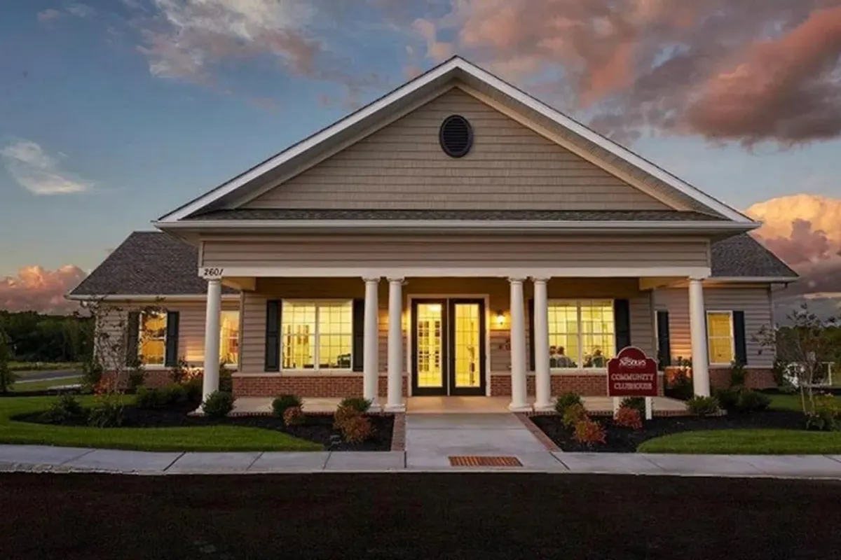 Westrum Corporate Single-story building with columns, lit warmly from inside, at dusk with a sign reading “Community Clubhouse” on the lawn.