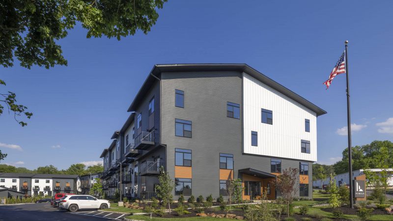 Westrum Corporate Foundry Flats is a modern three-story apartment building with cars parked outside, landscaped grounds, and an American flag on a sunny day.