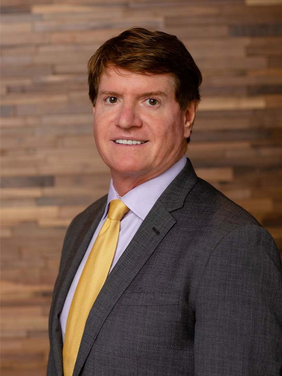 Westrum Corporate John Westrum, in a gray suit and yellow tie, smiles while standing before a wooden background.
