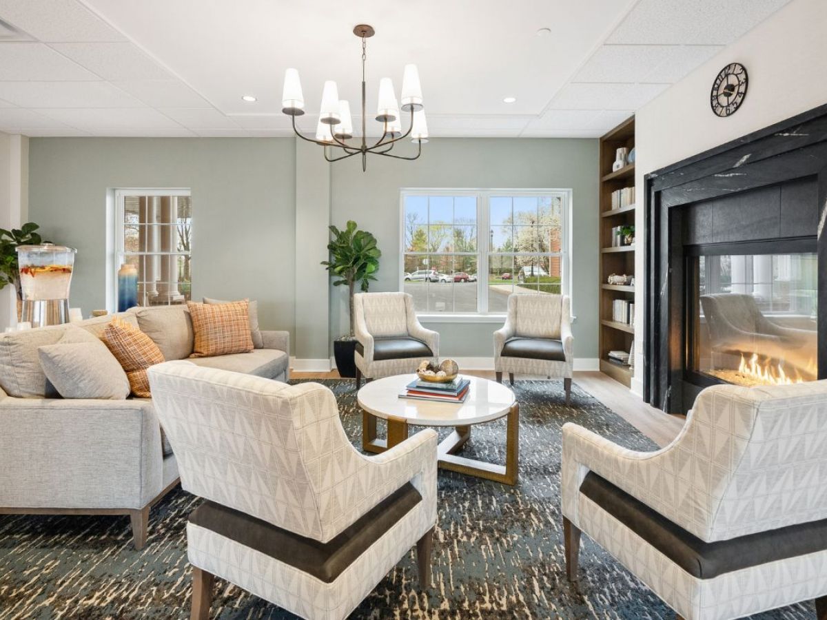 Westrum Corporate Modern Harleysville living room with four armchairs, a sofa, round coffee table, fireplace, chandelier, and large window.
