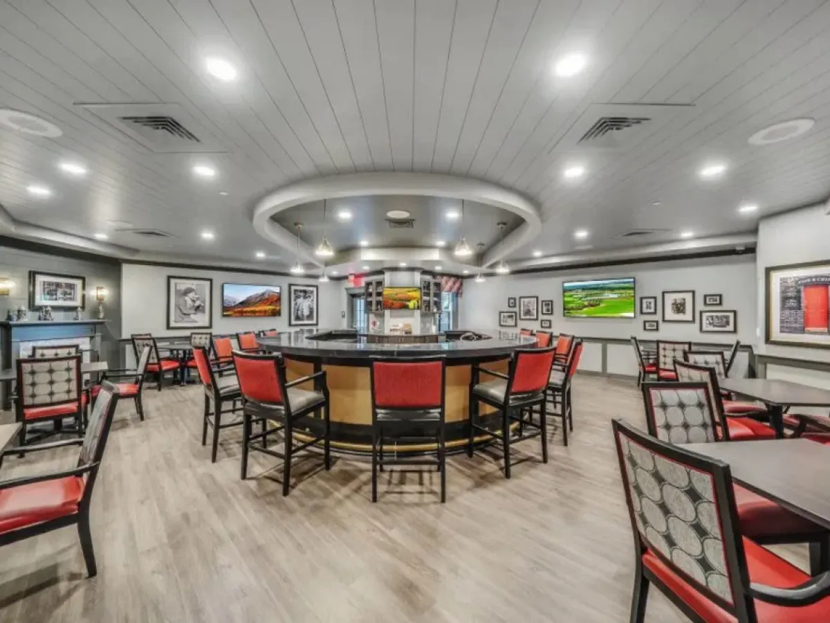 Westrum Corporate Modern dining area at Pinnacle at Plymouth Meeting, with red chairs, central bar, framed art, and TVs—perfect for luxury apartment living.