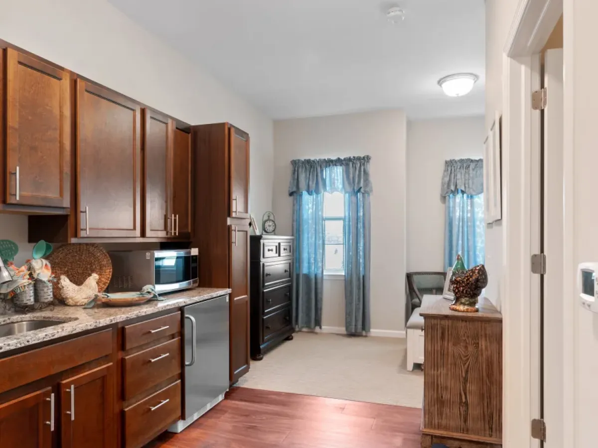 Westrum Corporate Cozy small kitchen at Arbour Square, West Chester—perfect for senior living with brown cabinets, granite countertop, and blue curtains.