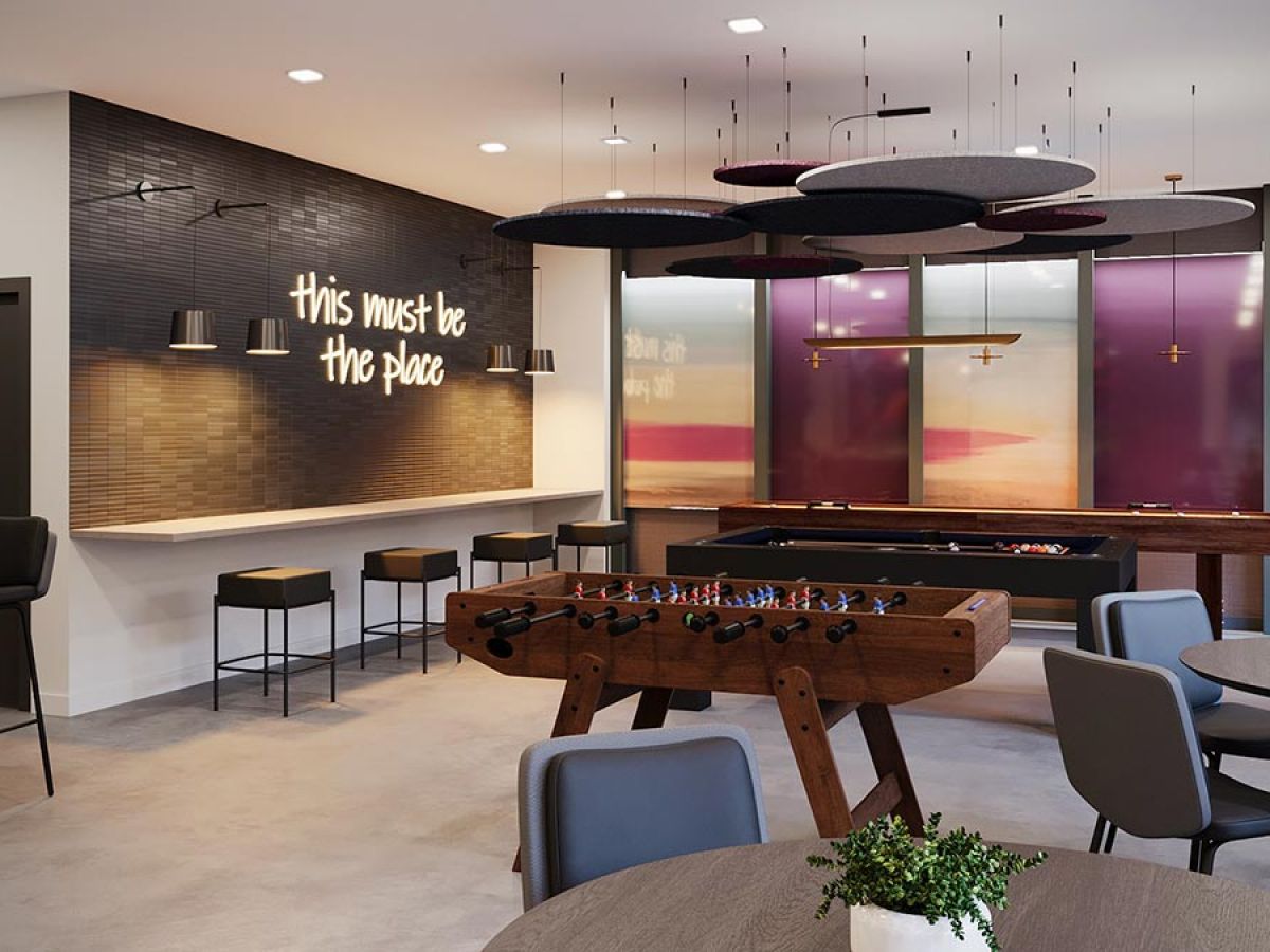 Westrum Corporate Modern game room at Luxor with foosball, pool tables, round tables, chairs, and a neon “This must be the place” sign.