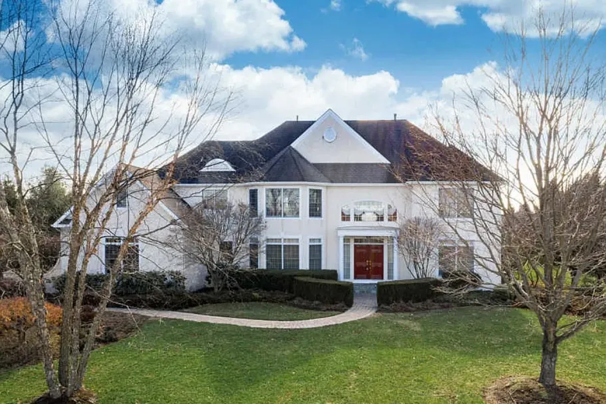 Westrum Corporate Large two-story white house in Hopewell Township with red double doors, front lawn, bare trees, and a curved walkway under a blue sky.