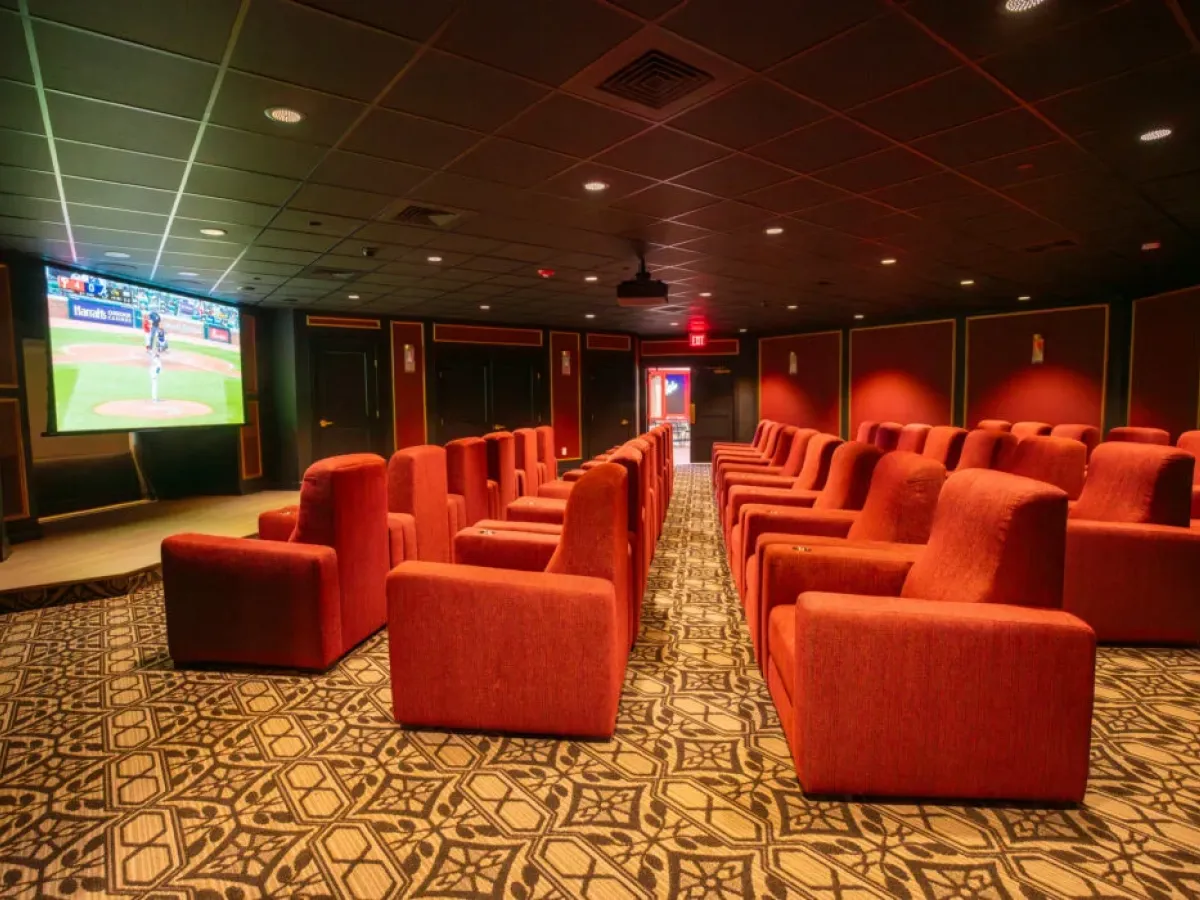 Westrum Corporate A theater room in Cinnaminson with rows of red cushioned seats faces a large screen showing a baseball game.