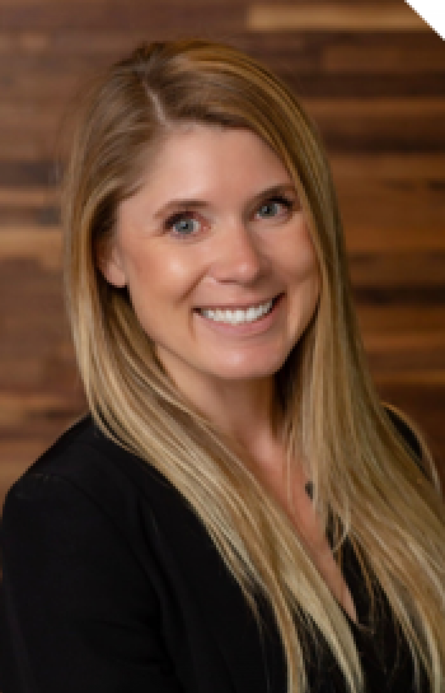 Westrum Corporate Smiling woman with long blonde hair wearing a black top, standing in front of a wooden background at the John Westrum event.