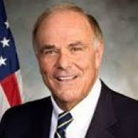 Westrum Corporate Edward G. Rendell, smiling in a suit and striped tie, poses confidently before an American flag and a neutral background.