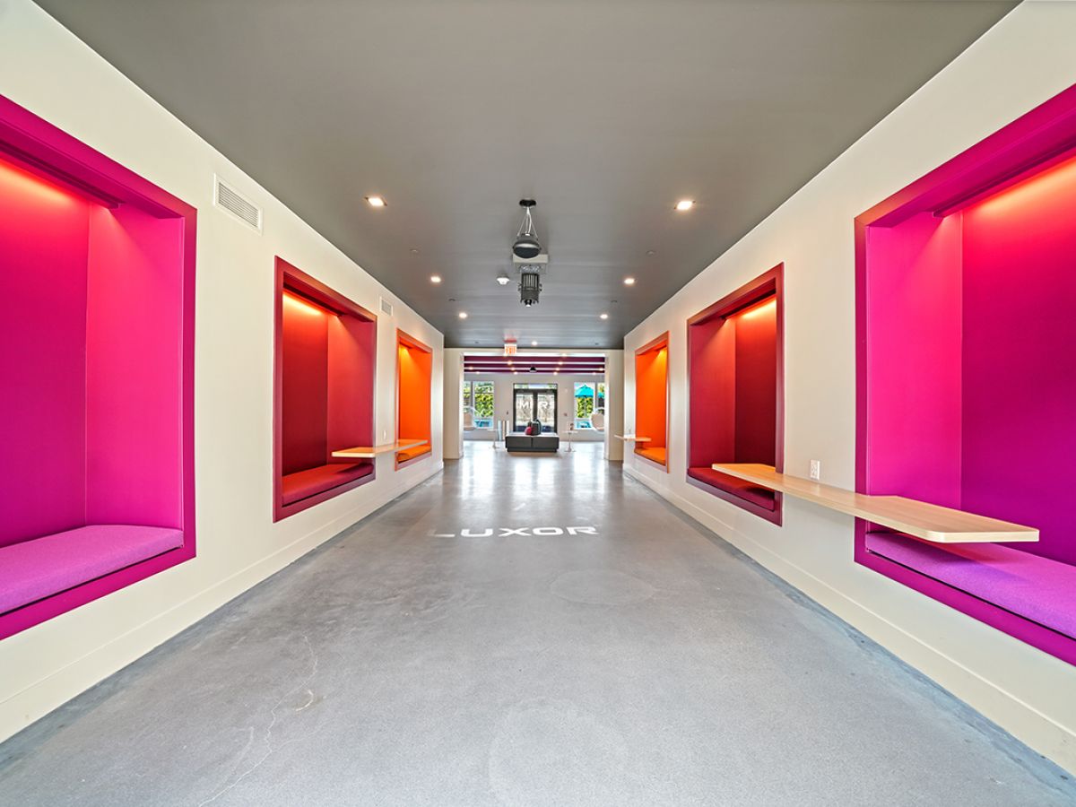 Westrum Corporate Bright hallway in Luxor features vibrant magenta and orange alcoves with benches, leading to glass doors at the far end.