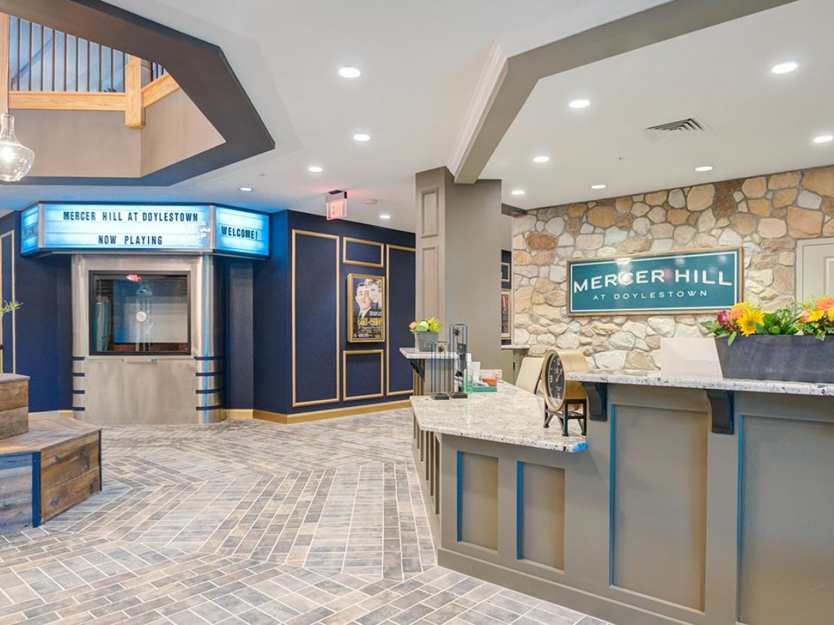 Westrum Corporate Bright Mercer Hill lobby features a stone wall, theater-style sign, ticket booth, gray desk, and vibrant flower arrangements.
