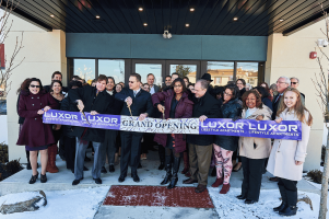 Westrum Corporate A group of people stand outside a building cutting a ribbon that says "Luxor Grand Opening Lifestyle Apartments.