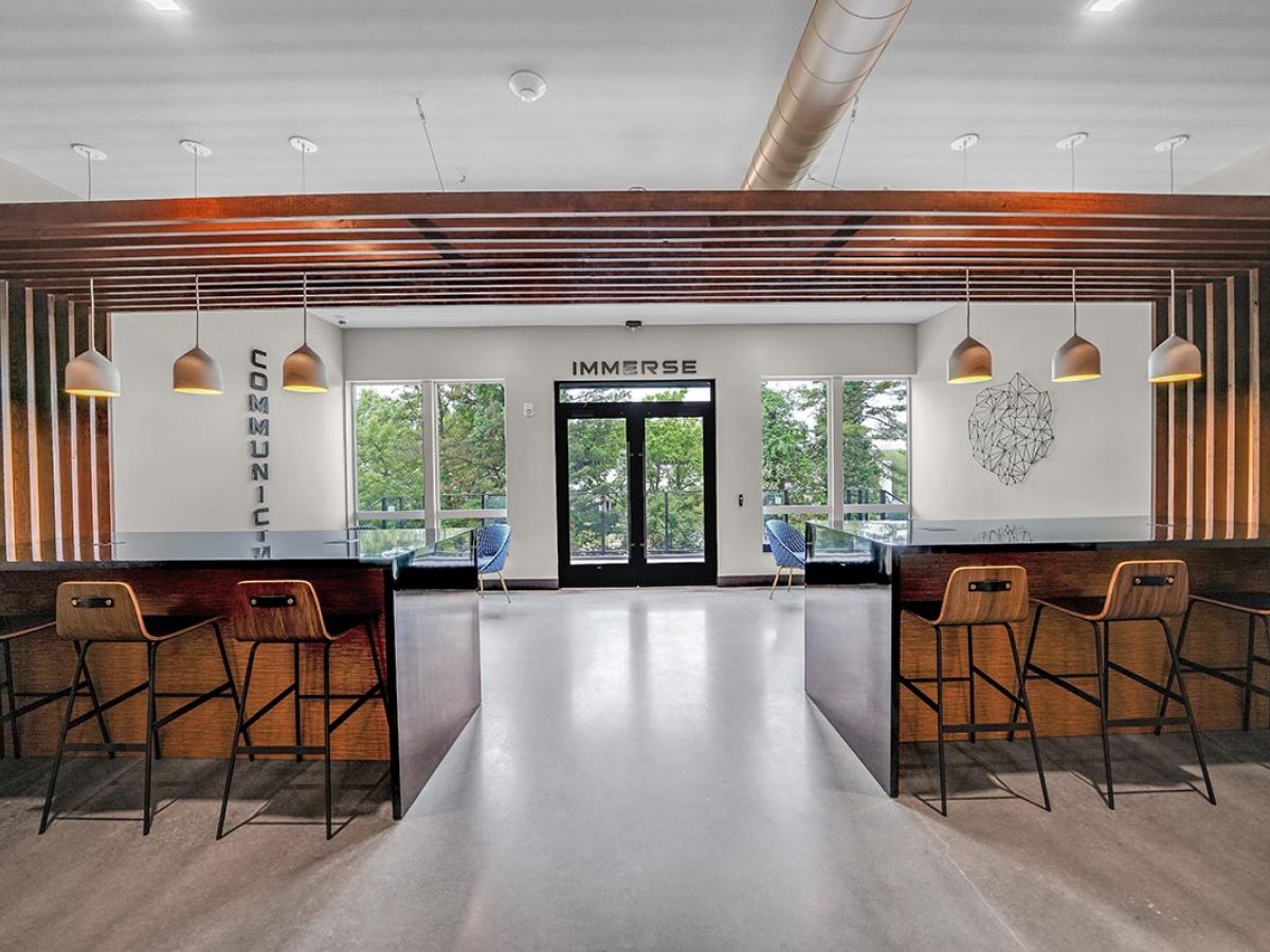 Westrum Corporate Modern common area at Luxor West Chester with wooden accents, bar seating, pendant lights, and large windows by the “IMMERSE” double door.