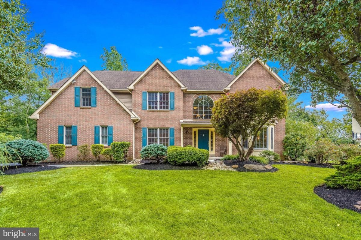 Westrum Corporate Two-story brick house in Ballantrae Woods with manicured shrubs, large windows, and central arched entry under a bright blue sky.