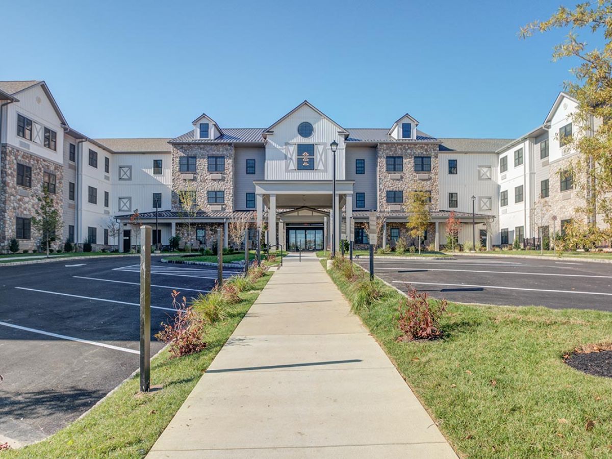 Westrum Corporate Wide sidewalk leads to Mercer Hill, a large modern building in Doylestown, with stone accents and greenery under a clear sky.