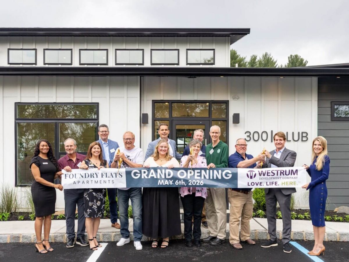 Westrum Corporate Thirteen people stand in front of a building holding a "Grand Opening" banner with the date May 6th, 2026, and smiling at the camera.