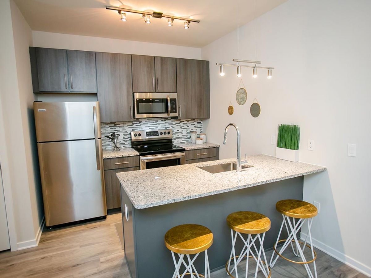 Westrum Corporate Modern kitchen at The Hub at 31 Brewerytown with stainless steel appliances, gray cabinets, granite island, and gold stools.