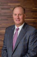 Westrum Corporate Smiling man in a plaid suit and pink tie poses in front of a wood-paneled background.