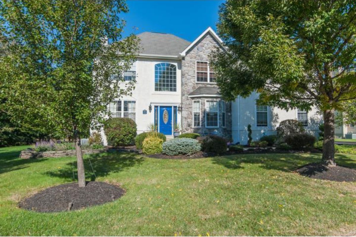 Westrum Corporate This Cambridge Knoll two-story home features a stone and white exterior, blue front door, large windows, and landscaped yard with trees.